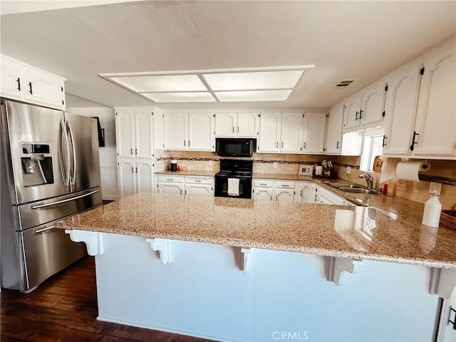 kitchen with visible vents, white cabinetry, a sink, a peninsula, and black appliances