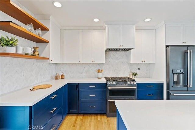 kitchen with blue cabinets, premium appliances, exhaust hood, and white cabinetry