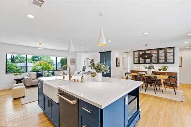 kitchen featuring visible vents, blue cabinetry, light countertops, light wood-style floors, and dishwasher