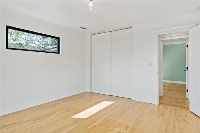 unfurnished bedroom featuring a closet, light wood-style flooring, and baseboards