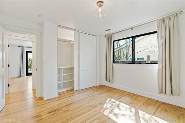 unfurnished bedroom featuring a closet, visible vents, baseboards, and wood finished floors