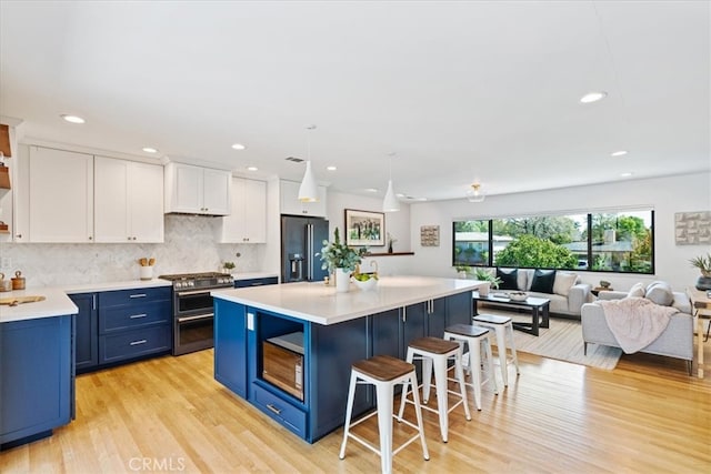 kitchen with blue cabinets, a breakfast bar, open shelves, black fridge with ice dispenser, and range with two ovens