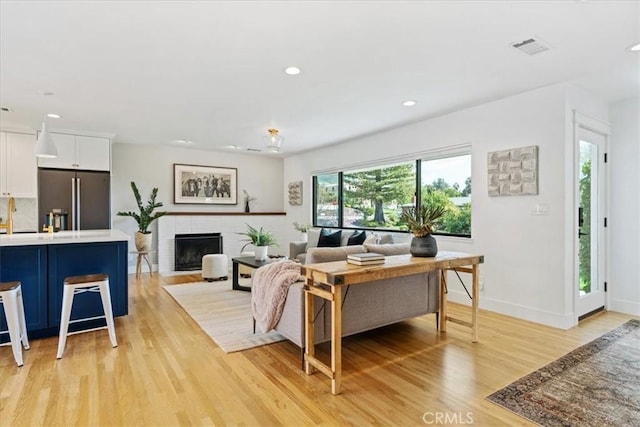 living room with recessed lighting, light wood-type flooring, a brick fireplace, and visible vents