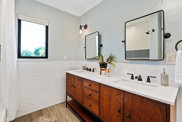 full bath featuring double vanity, wainscoting, wood finished floors, tile walls, and a sink