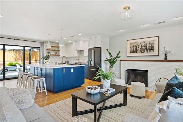 living area with a brick fireplace, light wood-style flooring, recessed lighting, and visible vents