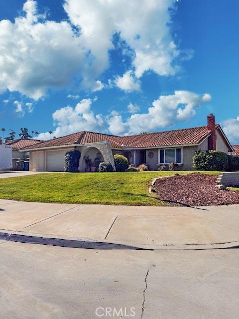 view of front of house featuring a garage, a tile roof, concrete driveway, and a front yard