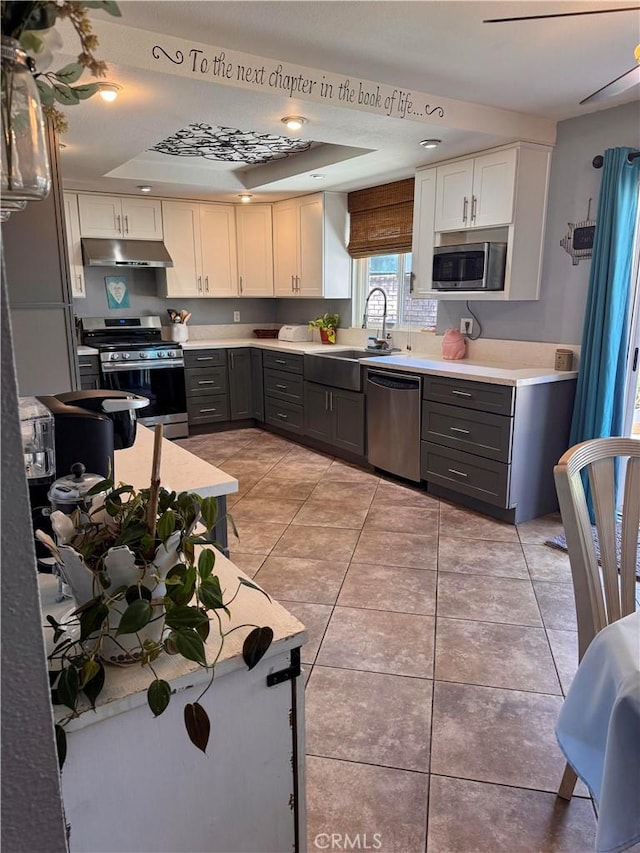 kitchen featuring light tile patterned floors, under cabinet range hood, stainless steel appliances, a sink, and gray cabinets