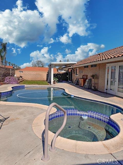 view of swimming pool with french doors, a patio area, fence, and a pool with connected hot tub