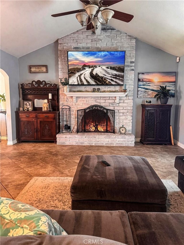 living room with a brick fireplace, arched walkways, vaulted ceiling, and a ceiling fan