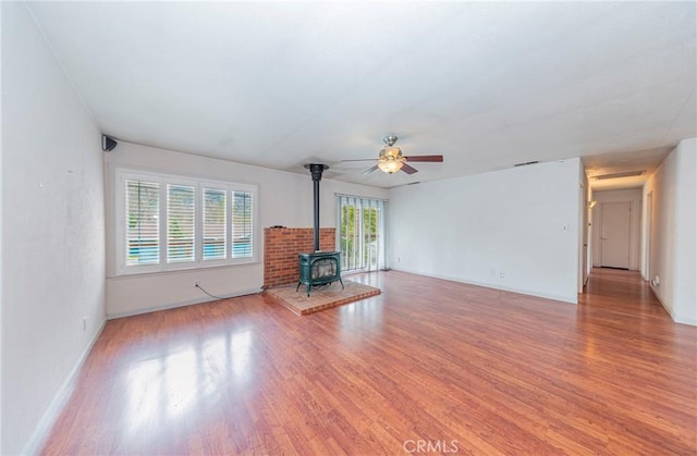 unfurnished living room with a wood stove, light wood-style floors, baseboards, and visible vents