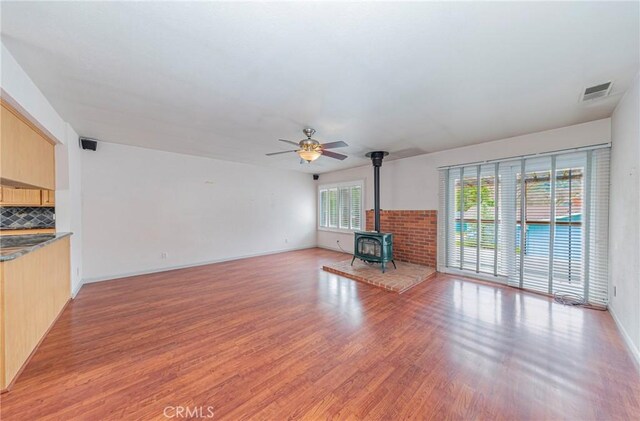 unfurnished living room featuring visible vents, baseboards, ceiling fan, a wood stove, and light wood-type flooring