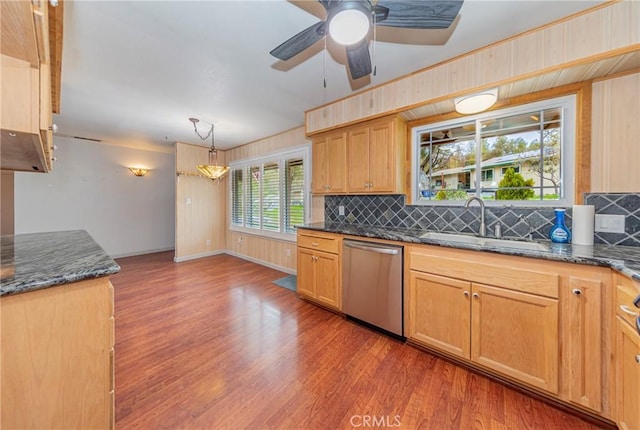 kitchen with dark stone counters, a sink, dishwasher, light wood finished floors, and tasteful backsplash