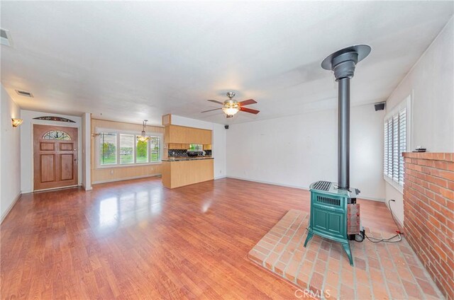 unfurnished living room with visible vents, light wood-style flooring, a wood stove, and a ceiling fan