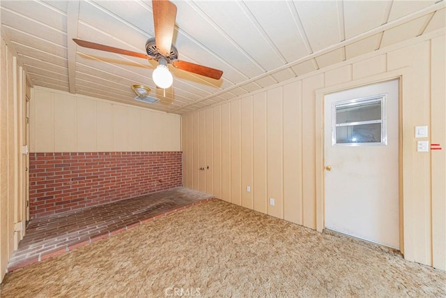 unfurnished room with a ceiling fan, carpet, and wood walls