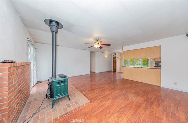 living area featuring a wood stove, ceiling fan, and light wood-style flooring