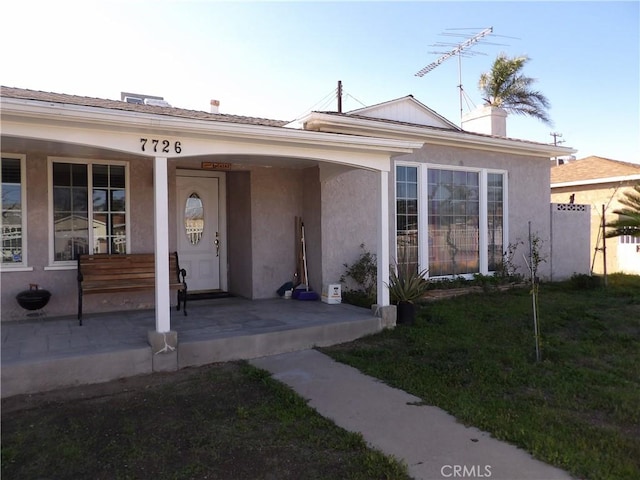 view of front facade featuring covered porch, a front yard, and stucco siding