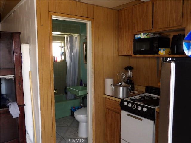 kitchen with range with gas stovetop, brown cabinetry, freestanding refrigerator, black microwave, and tile patterned floors