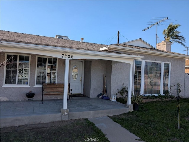 view of front of house with a porch, a chimney, and stucco siding