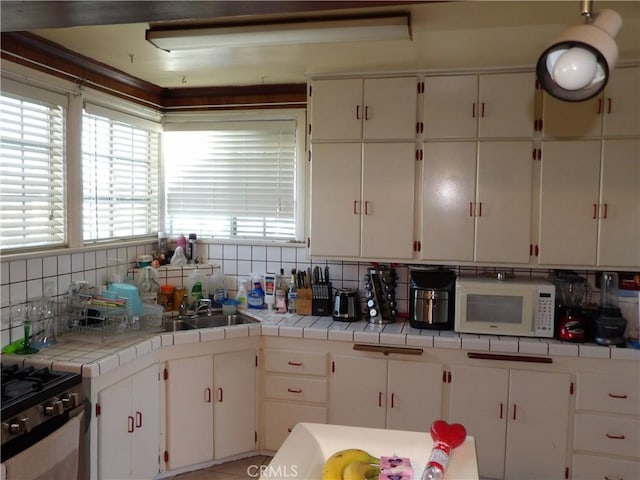 kitchen with tasteful backsplash, white microwave, gas stove, white cabinetry, and a sink