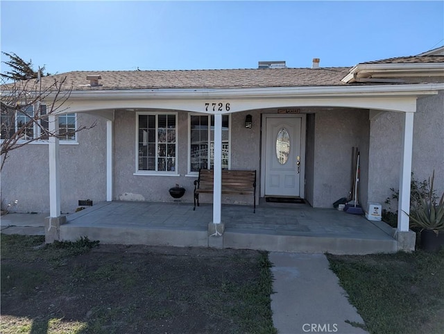 doorway to property featuring roof with shingles, a porch, and stucco siding