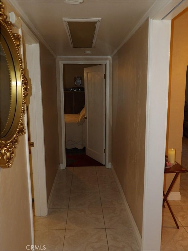 hallway with attic access, light tile patterned flooring, ornamental molding, and baseboards