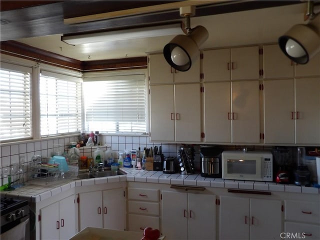 kitchen featuring white cabinetry, a sink, backsplash, and white microwave