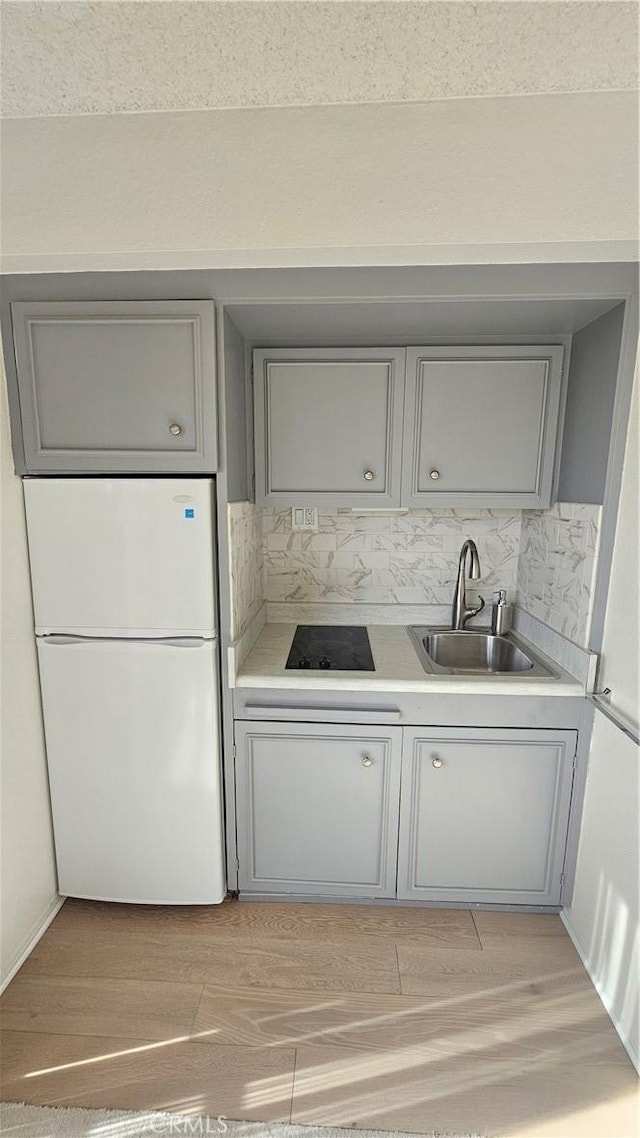 kitchen featuring gray cabinetry, light countertops, light wood-style flooring, freestanding refrigerator, and a sink