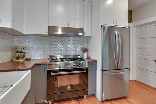 kitchen featuring under cabinet range hood, butcher block countertops, decorative backsplash, white cabinets, and stainless steel appliances