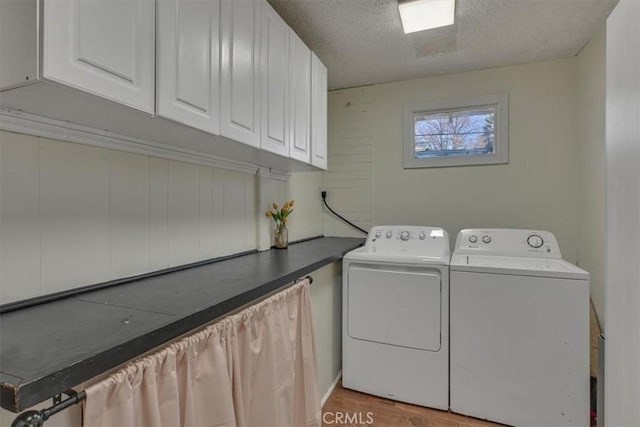 laundry room featuring light wood-type flooring, cabinet space, independent washer and dryer, and a textured ceiling