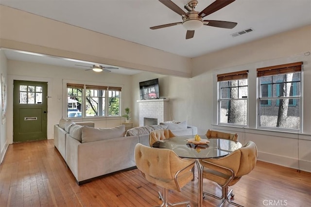 dining room with visible vents, a brick fireplace, baseboards, light wood-style flooring, and a ceiling fan