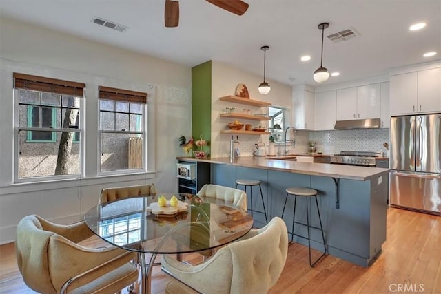 kitchen featuring under cabinet range hood, visible vents, freestanding refrigerator, and a sink