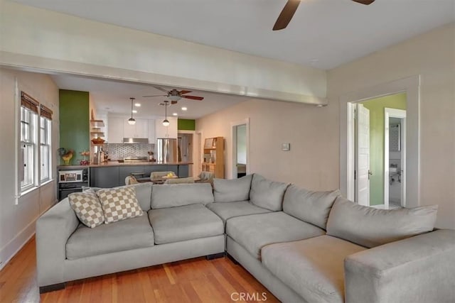 living room featuring light wood finished floors, baseboards, and a ceiling fan