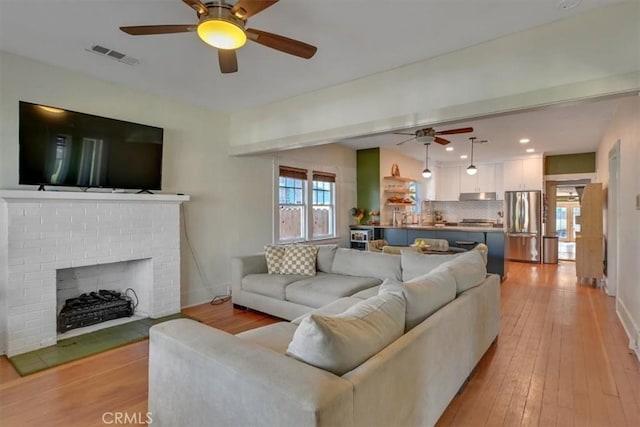 living area featuring visible vents, a fireplace, light wood-type flooring, and baseboards