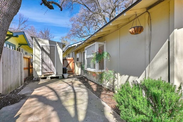 view of property exterior with a storage shed, an outdoor structure, fence, and a patio