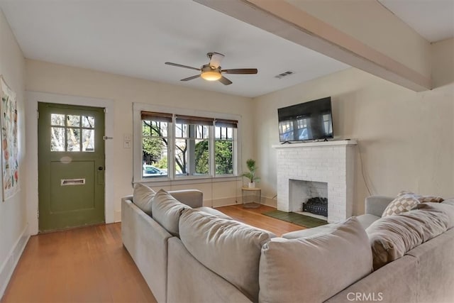 living room featuring visible vents, light wood finished floors, baseboards, a brick fireplace, and ceiling fan