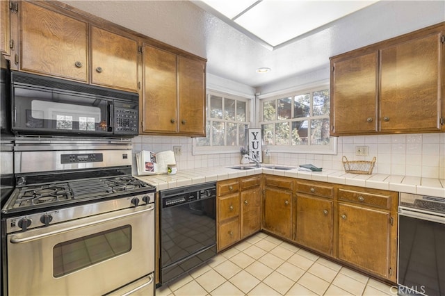 kitchen with a sink, backsplash, black appliances, and light tile patterned floors