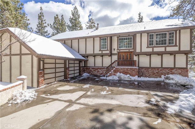 snow covered rear of property with a garage, concrete driveway, brick siding, and stucco siding