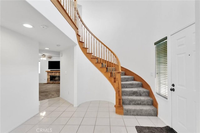 carpeted entrance foyer featuring tile patterned flooring, a fireplace, stairway, and ceiling fan