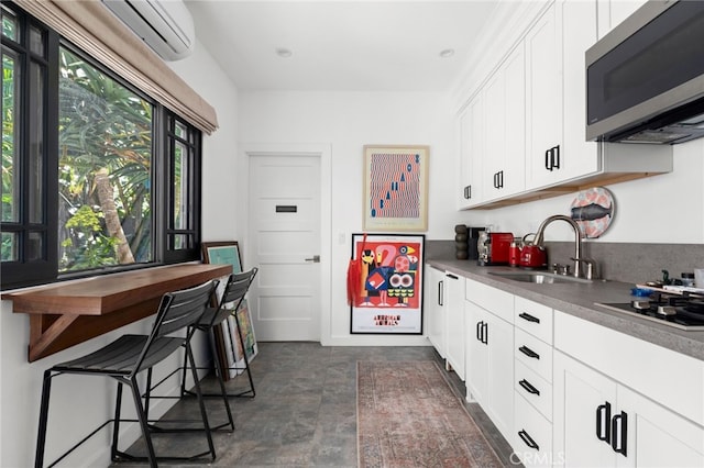 kitchen featuring stainless steel microwave, a wall mounted air conditioner, white cabinetry, gas cooktop, and a sink