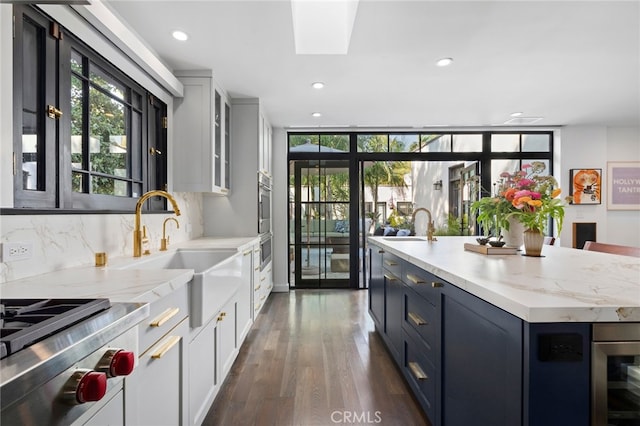 kitchen featuring a sink, white cabinetry, a skylight, decorative backsplash, and dark wood-style flooring