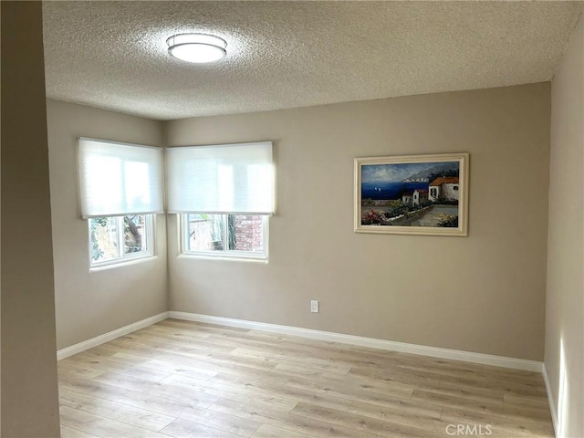 spare room featuring light wood-style flooring, baseboards, and a textured ceiling