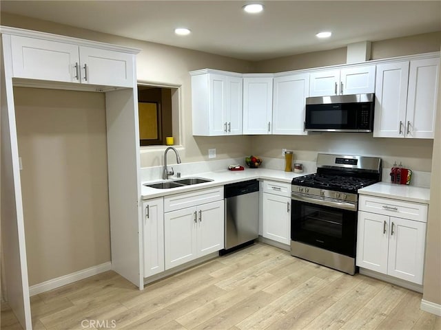 kitchen featuring white cabinets, appliances with stainless steel finishes, light countertops, light wood-type flooring, and a sink