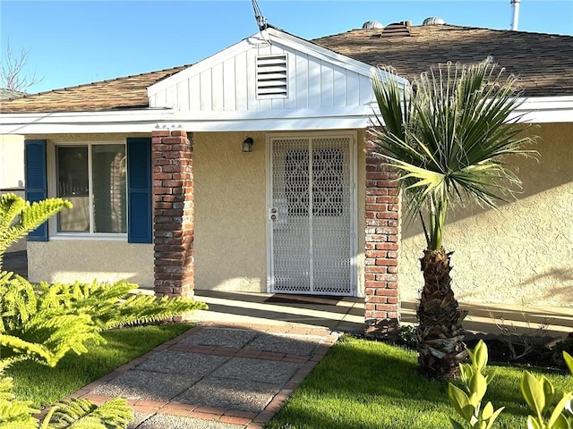 doorway to property featuring stucco siding, a shingled roof, and brick siding