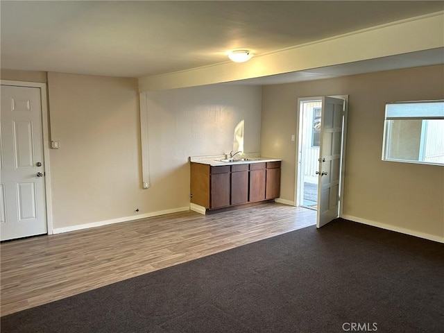 carpeted empty room featuring baseboards, a sink, and wood finished floors