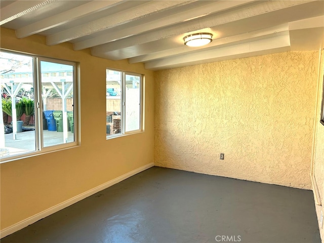 unfurnished room with concrete floors, baseboards, and beamed ceiling