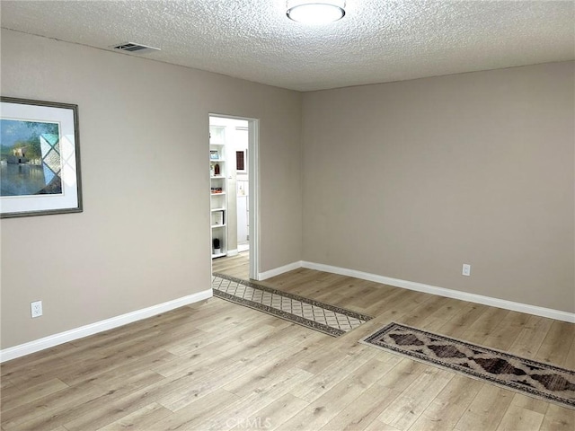 spare room with hardwood / wood-style flooring, baseboards, visible vents, and a textured ceiling