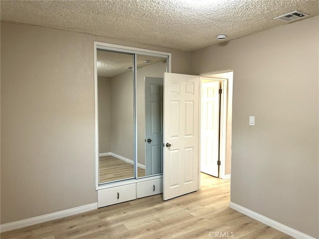 unfurnished bedroom featuring baseboards, a textured ceiling, visible vents, and light wood-style floors