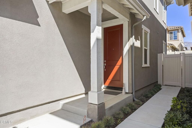 view of exterior entry featuring fence and stucco siding