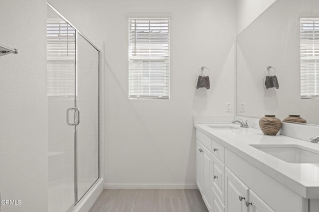 full bath with double vanity, a stall shower, baseboards, and a sink