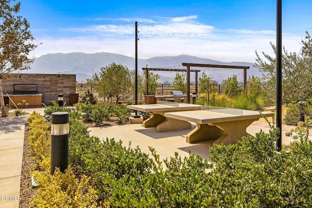 view of community featuring fence, a mountain view, an outdoor kitchen, and a patio